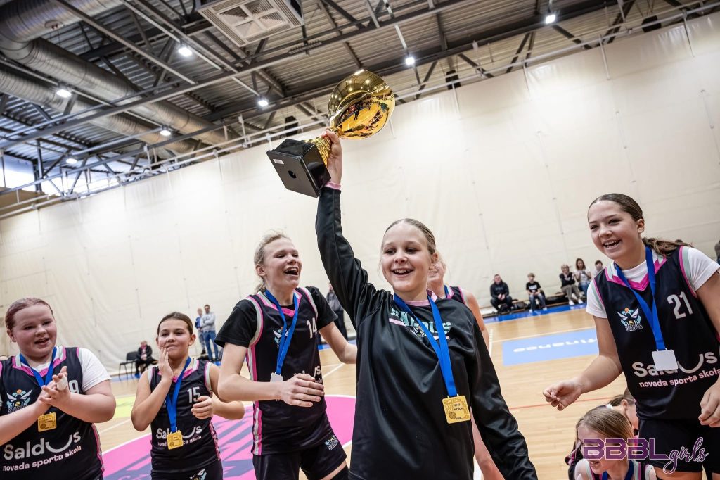 spēlētājas smaida, vienai rokās kauss pacelts virs galvas.