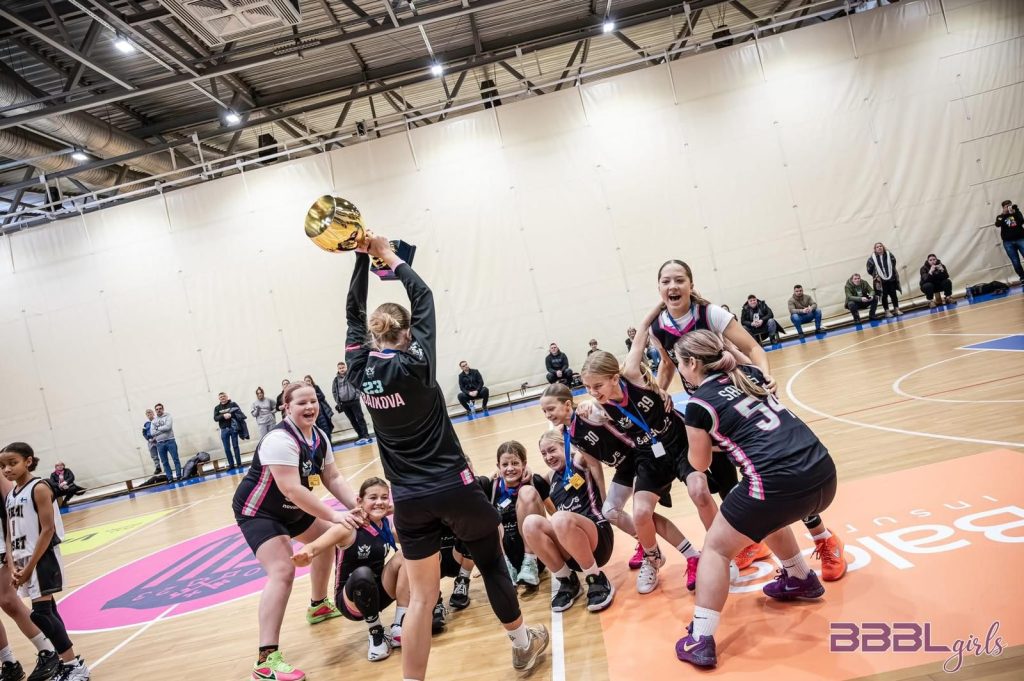 pēc spēles. viena no spēlētājām pacēlusi kausu virs galvas.