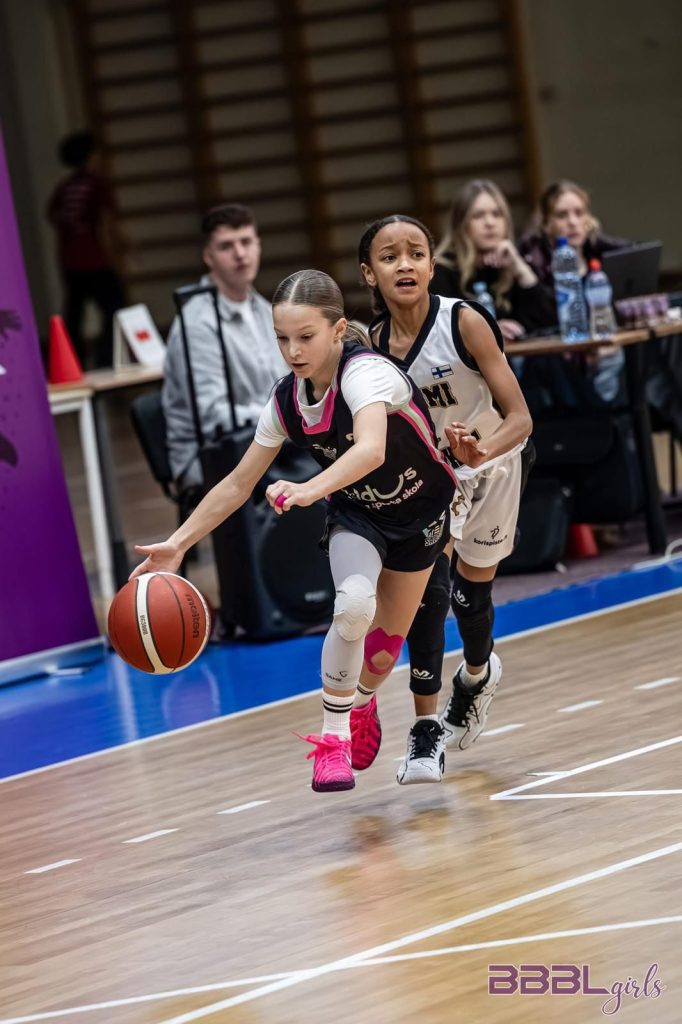 mūsu spēlētaja ar bumbu, pakaļ dzenas pretiniece no mugurpuses.