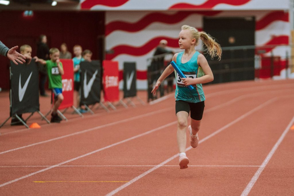 mūsu audzēkne skrien ar stafetes kociņu rokā
