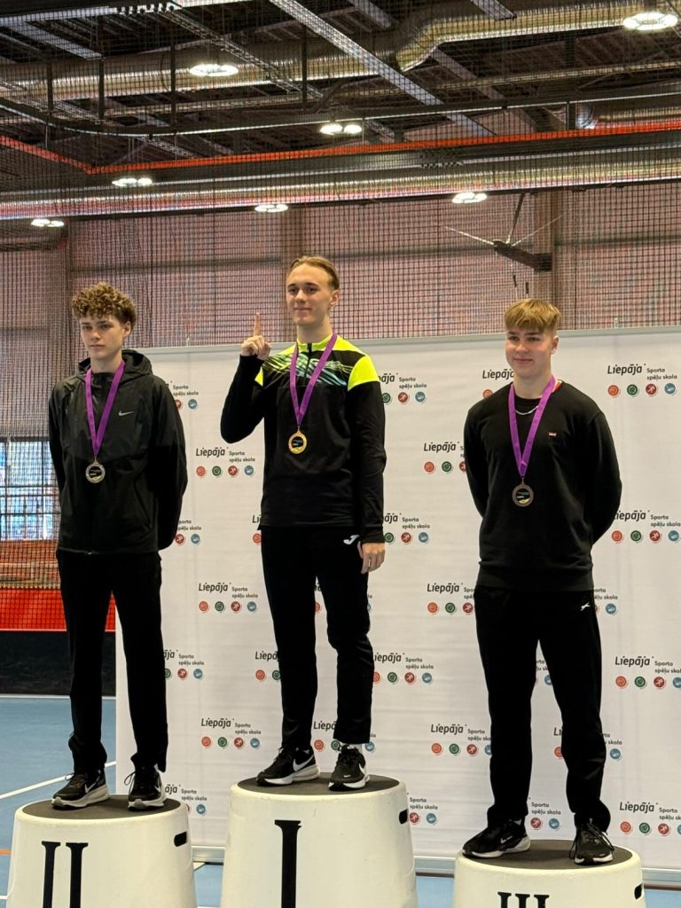 skats uz pjedestālu ar trīs puišiem, kuriem kaklā medaļas