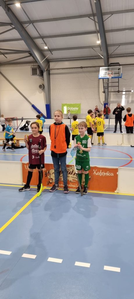 3 florbolisti stāv pie laukuma bortiem