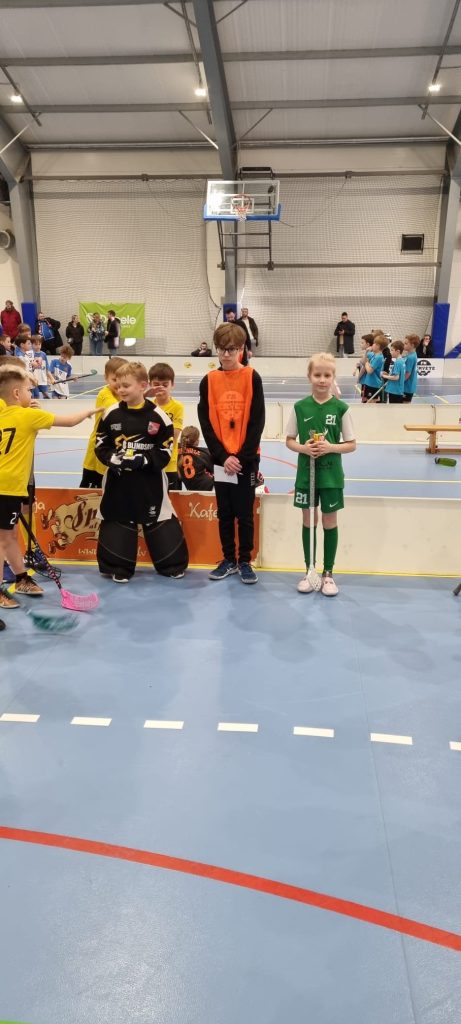 3 florbolisti stāv pie laukuma bortiem