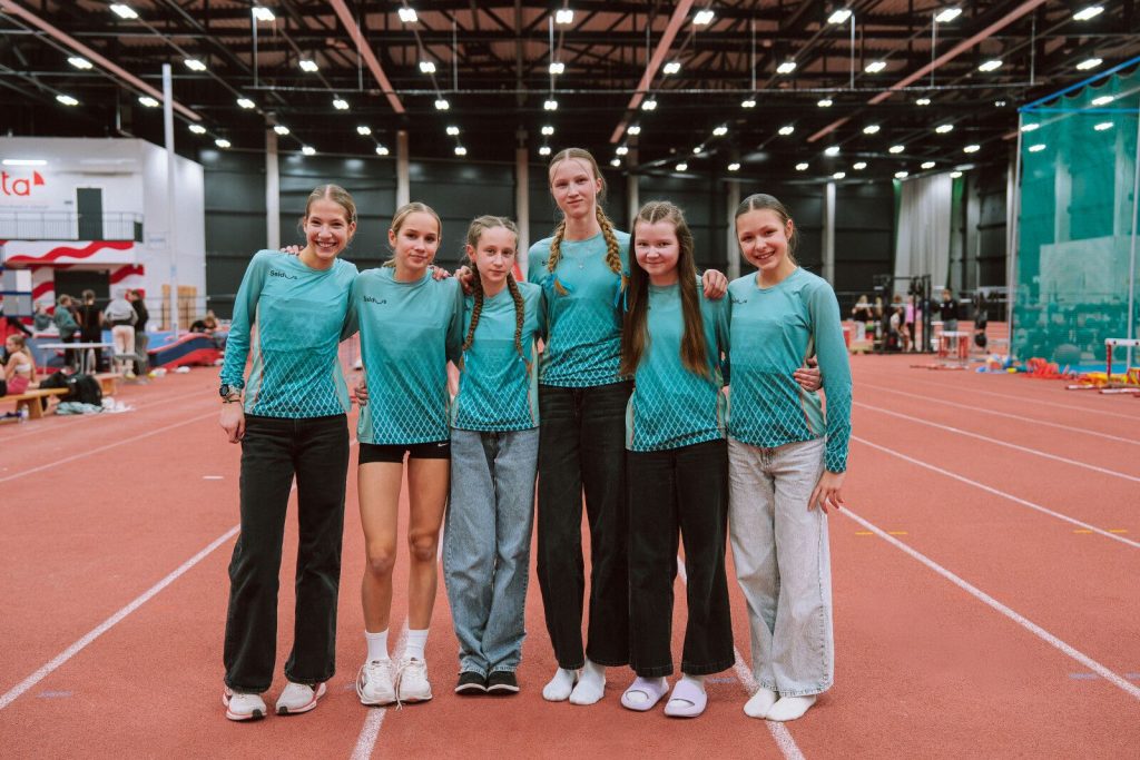 mūsu sportistes kopā saķērušās, pozē skriešanas sektorā