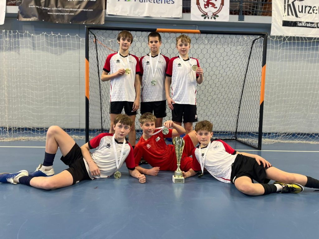 1.vietas ieguvēju kopbilde pie futbola vārtiem ar kausu un medaļām