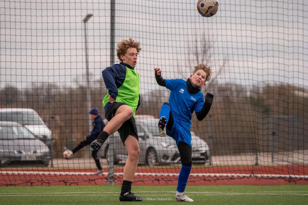 spēles epizode, diviem zēniem paceltas kājas, bumba gaisā.