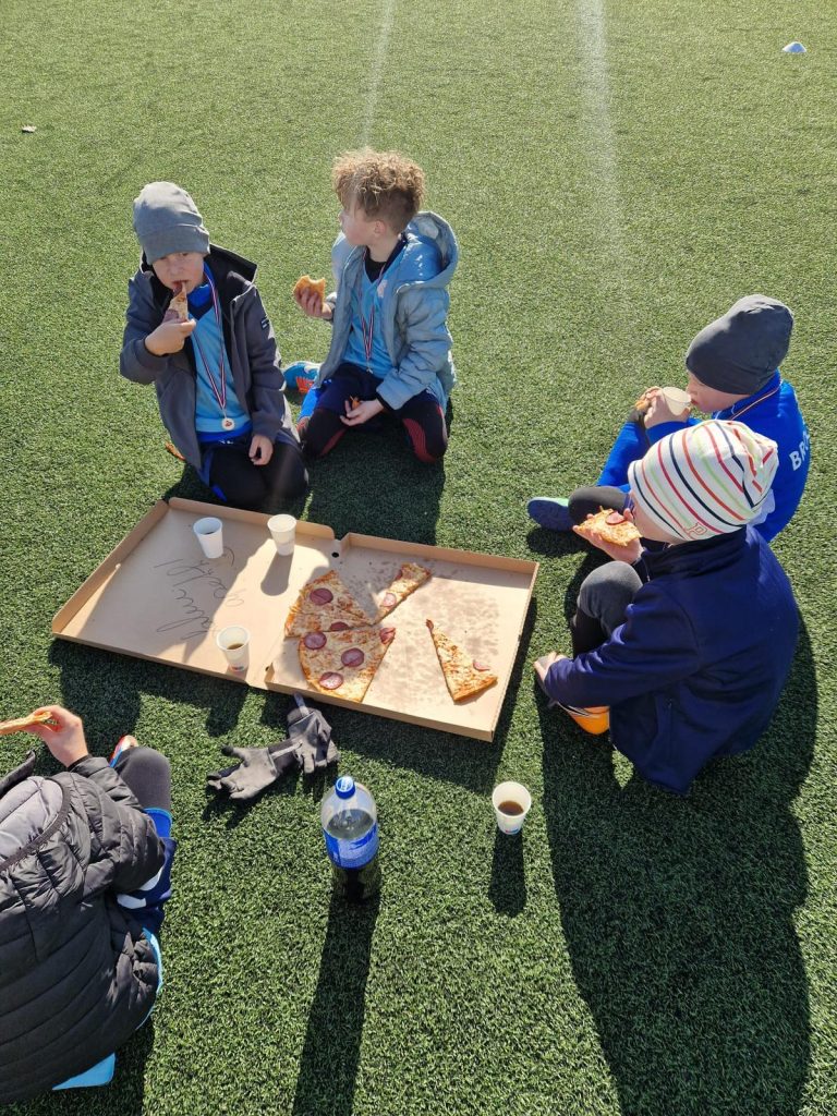 bērni ēd picu. Apsēdušies apkārt picas kastei.