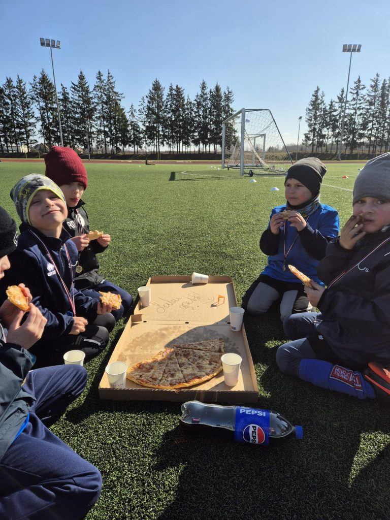 bērni sēž zālītē - laukuma malā. ēd picu.