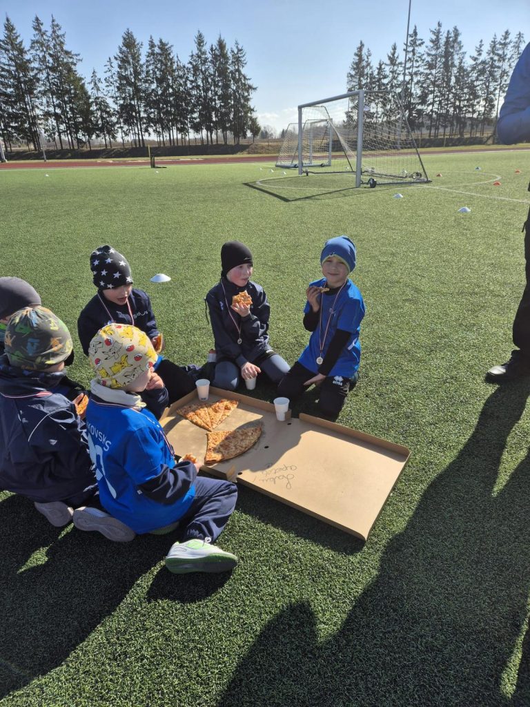 bērni sēž zālītē - laukuma malā. ēd picu.