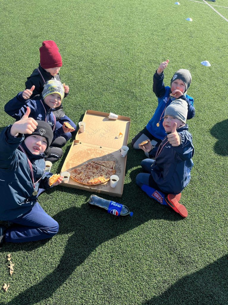 bērni atvēruši piocas kasti un ēd picu. Vairāk kā pusi picas jau apēduši.