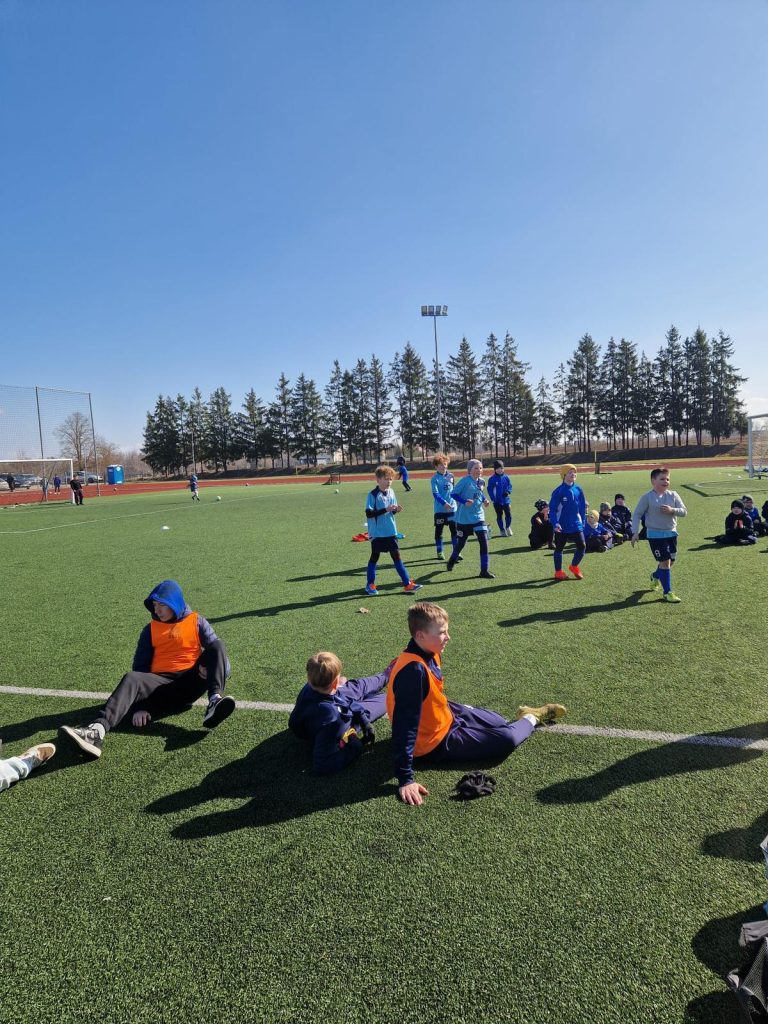 bērni uz laukuma. Daži sēž laukuma malā