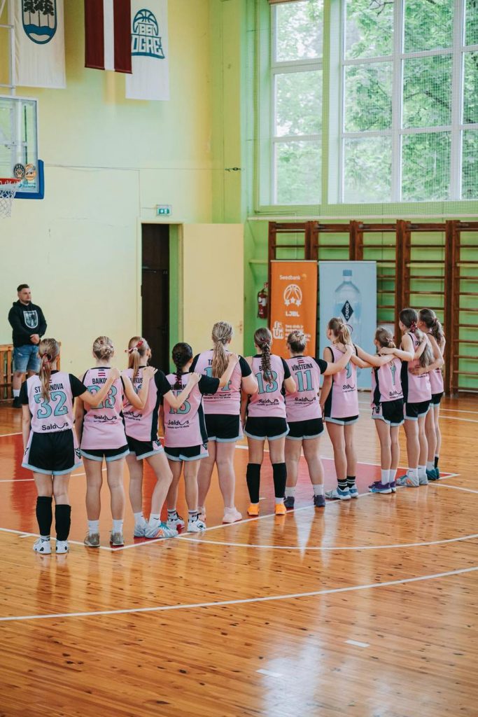 foto no mugurpuses. Mūsu basketbolistes apķērušās, stāvot vienā rindā