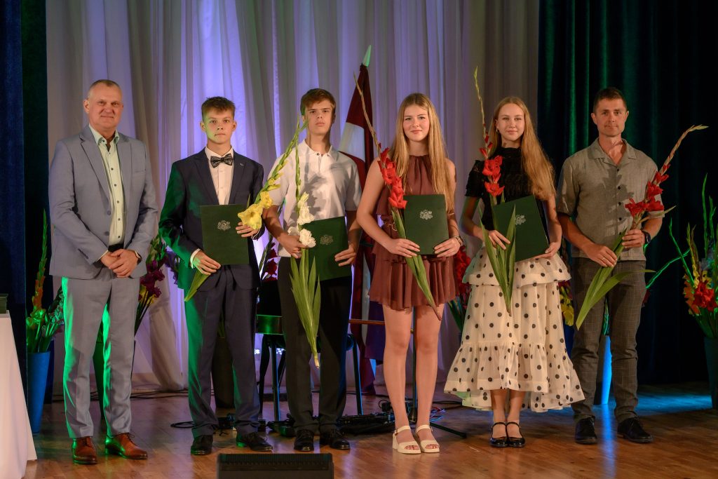 absolventu kopbilde ar ziediem un diplomiem rokās