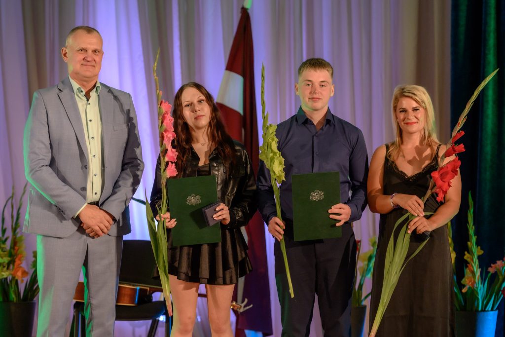 absolventu kopbilde ar ziediem un diplomiem rokās